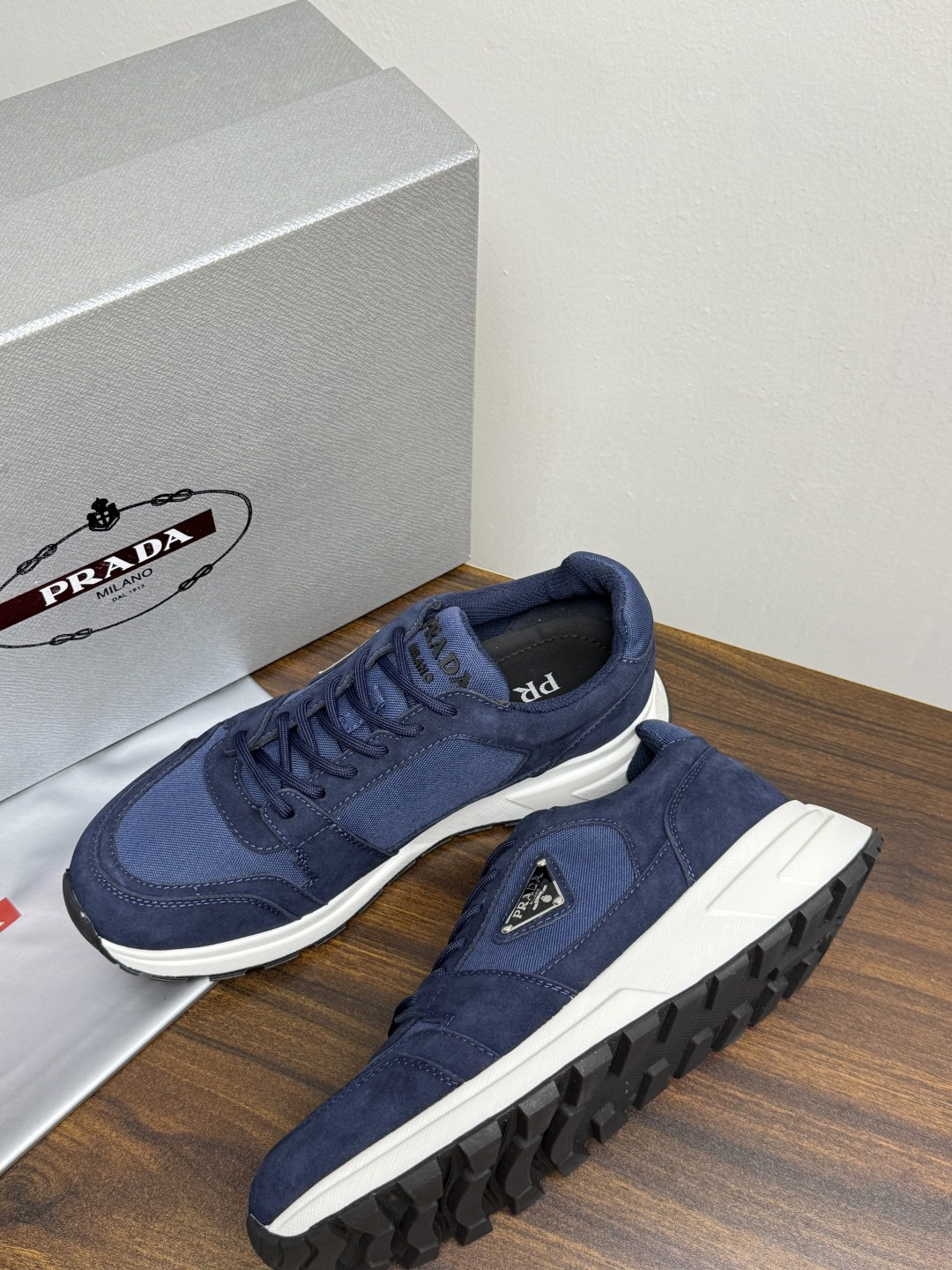 Prada Brush 运动鞋​​，鞋面是麂皮 + 尼龙织物拼接，侧面有 Prada 标志性的 三角珐琅金属标 ，厚底橡