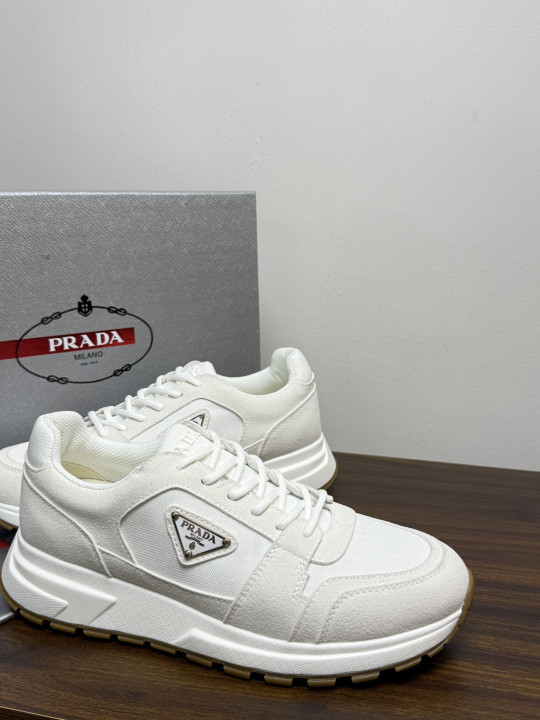 Prada Brush 运动鞋​​，鞋面是麂皮 + 尼龙织物拼接，侧面有 Prada 标志性的 三角珐琅金属标 ，厚底橡