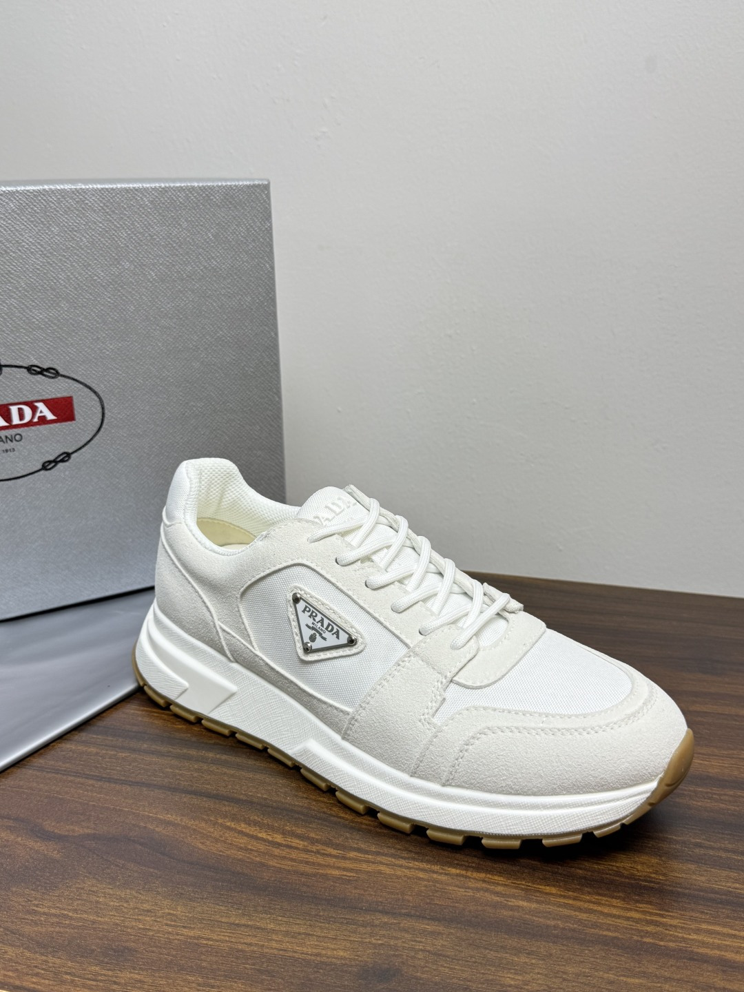 Prada Brush 运动鞋​​，鞋面是麂皮 + 尼龙织物拼接，侧面有 Prada 标志性的 三角珐琅金属标 ，厚底橡