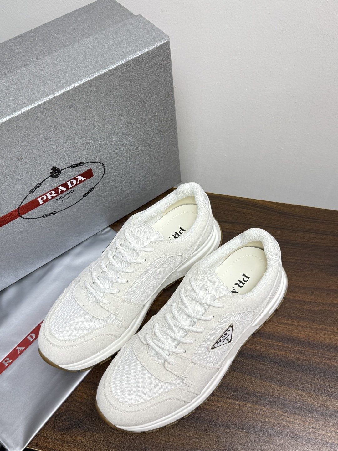 Prada Brush 运动鞋​​，鞋面是麂皮 + 尼龙织物拼接，侧面有 Prada 标志性的 三角珐琅金属标 ，厚底橡