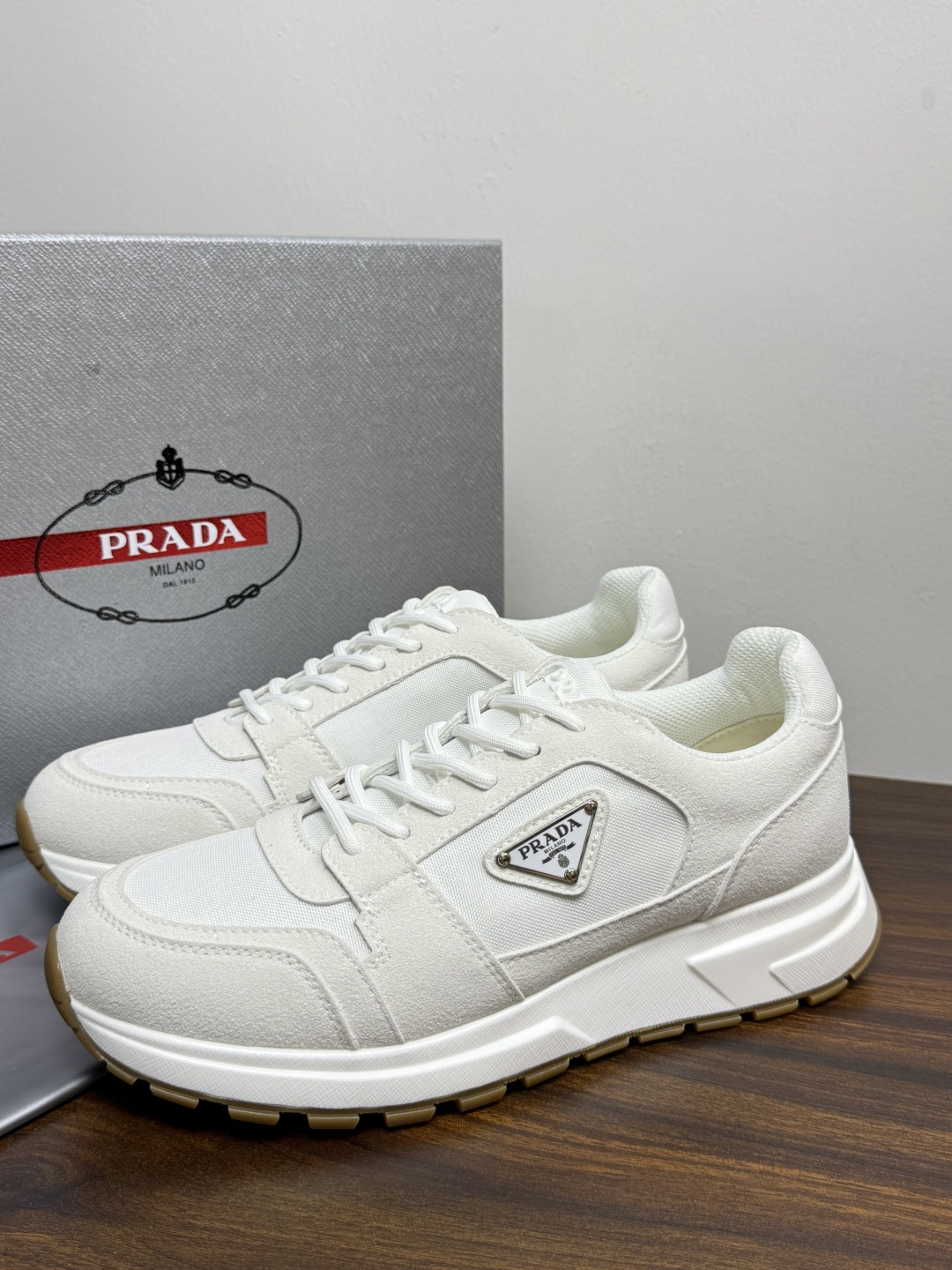 Prada Brush 运动鞋​​，鞋面是麂皮 + 尼龙织物拼接，侧面有 Prada 标志性的 三角珐琅金属标 ，厚底橡