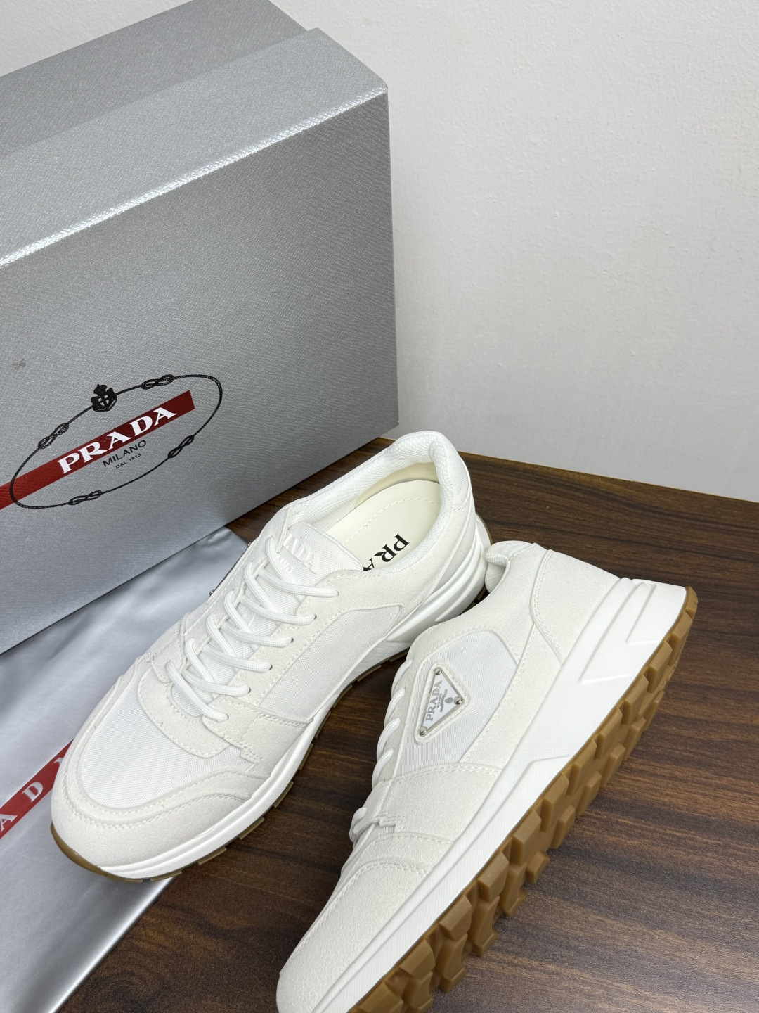 Prada Brush 运动鞋​​，鞋面是麂皮 + 尼龙织物拼接，侧面有 Prada 标志性的 三角珐琅金属标 ，厚底橡