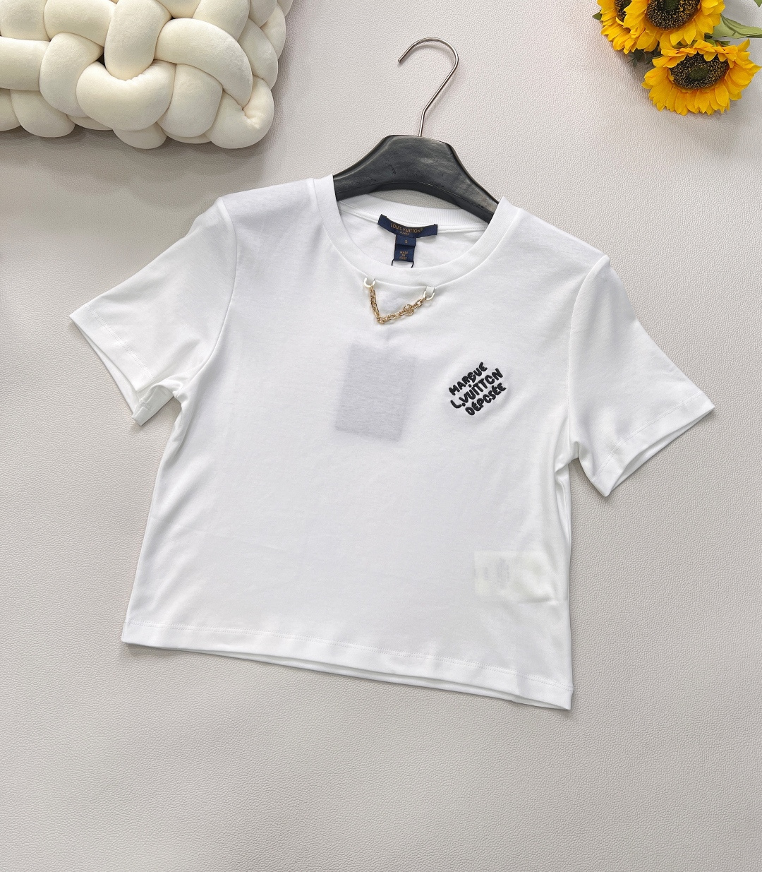 NO:421872,LOUIS VUITTON Chain letter embroidery short short-sleeved T-shirt with chain letter embroidery engraved, and the classic is written with stitches. Short-cut silhouette × Heavy industry embroidery Arrogant and elegant High-waist short-cut design accurately improves the waistline, and matches with high-waist bottoms to instantly lengthen the legs, easily grasping the balance rule of 'lazy and neat'. High-string combed cotton has a cloud-like touch, short-sleeved tailoring is neat and inclusive, and the silhouette supports the luxurious experience of not picking on the figure. Classic chain elements, paired with exquisite embroidery craftsmanship, every detail exudes nobility and elegance!  The top is made of plain color, decorated with four-leaf clover's iconic letter elements in the pocket, the neckline is wrapped in the chain details, making the simple style more layered, and the outfit is a casual and lazy style. Size sml code m,,louis vuitton,T-shirt,tees,t-shirt,alexander wang19860909LOUIS VUITTON 链条字母刺绣短款短袖T恤 锁链鎏金,刺绣铭刻,以针脚续写经典.  短裁廓形 × 重工刺绣 嚣张亦优雅 高腰短裁设计,精准提升腰线,搭配高腰下装即刻拉长腿型,轻松拿捏「慵懒与利落」的平衡法则.  高支精梳棉,触感如云,短袖剪裁利落包容,廓形撑起不挑身材的奢侈体验.  经典链条元素,搭配上精致的刺绣工艺,每一个细节都散发着高贵与优雅！ 上衣素色打底 饰以四叶草标志性字母元素于口袋 领口包边链条细节 让简单款式更显层次感 穿搭出休闲慵懒风格 尺码sml 编码m,,louis vuitton,T-shirt,tees，t-shirt,alexander wang,Women's clothing