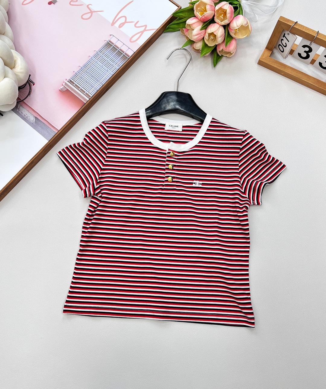 NO:448155,CELINE's new striped logo embroidered logo short-sleeved T-shirt. This T-shirt is mainly red and black stripes. The classic striped elements have a retro charm. The width and color scheme of the stripes have been carefully designed, which is very layered visually. Whether worn alone or as an inner layer, it can be easily highlighted. The white border at the neckline looks like a delicate picture frame, outlining the beautiful lines on the neck, simple and playful. The exquisite embroidery logo at the front chest  The logo is like the brightest star in the night sky, showing the noble identity of the brand in a low-key manner. The three gold buttons are the finishing touch, adding a touch of luxury to the whole, making the simple T-shirt unique in an instant. This T-shirt is made of high-quality cotton fabric, with a soft and delicate touch, as if a cloud touches the skin, bringing the ultimate wearing experience. Good breathability and moisture absorption can keep you dry and comfortable even in the hot summer. The fabric has been specially treated and is not easy to deform and fade, and it will still be new for a long time. The three standards are complete, and the large-scale product is size sml code, celine, T-shirt, tees, t-shirt, alexander wang19860909CELINE新款条纹logo刺绣徽标短袖T恤.这款T恤以红黑条纹为主调,经典的条纹元素自带复古韵味,条纹的宽窄与配色经过精心设计,视觉上极具层次感,无论单穿还是作为内搭,都能轻松出彩.领口处的白色镶边,似精致的画框,勾勒出颈部的优美线条,简约又不失俏皮.前胸处精致的刺绣 logo 徽标,宛如夜空中最闪亮的星,低调中彰显着品牌的高贵身份.三颗金色纽扣更是点睛之笔,为整体增添了一抹奢华质感,让简约的T恤瞬间变得与众不同.这款T恤采用高品质棉质面料,触感柔软细腻,仿佛是云朵轻触肌肤,带来极致的穿着体验.良好的透气性和吸湿性,即使在闷热的夏日,也能让你保持干爽舒适.面料经过特殊处理,不易变形和褪色,长久穿着依然如新.三标齐全,大货出 尺码sml 编码,,celine,T-shirt,tees，t-shirt,alexander wang,Women's clothing
