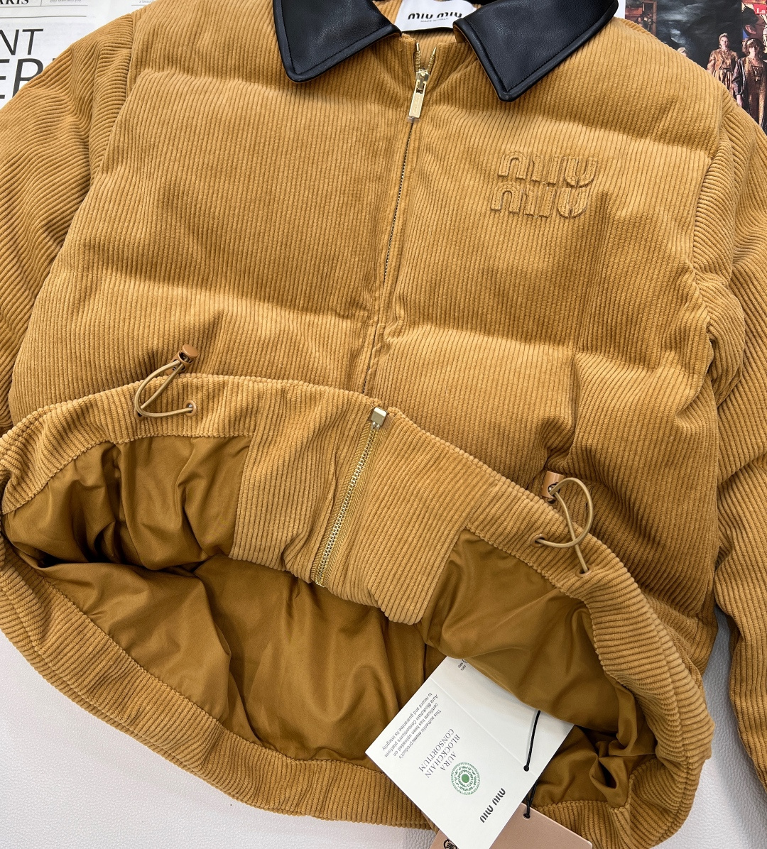 🆕 MIUMIU 暖色灯芯绒皮翻领拉链羽绒服，采用灯芯绒面料，手感柔软细腻，保暖性良好。同时，灯芯绒的表