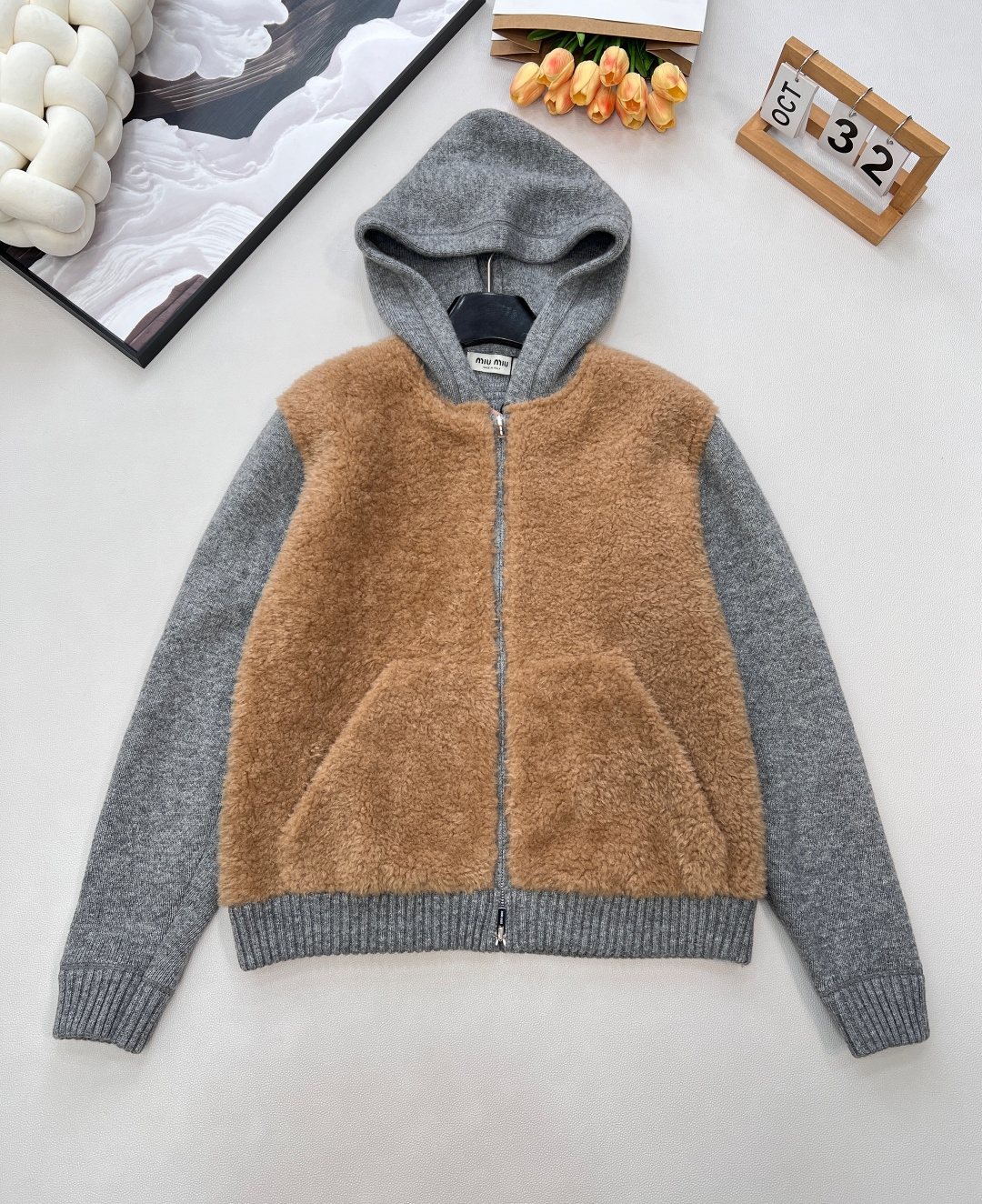 NO:590120,Miumiu's new all-in-one hooded knitted cardigan with lamb wool is made of innovative splicing of lamb wool and knitted fabrics. Camel-colored lamb wool is laid on the main body of the garment. It is fluffy and soft as clouds against the skin, instantly filling the winter atmosphere. The smoke gray knitted cardigan extends to the hood, cuffs and hem. The delicate knitted texture has a retro accent, and the collision of the two materials is striking.  The hooded design adds a bit of casualness and laziness, and the two-way zipper makes it easy to put on and take off and create multiple shapes. The pockets on both sides are practical and hidden. From the fabric to the craftsmanship, Miu Miu's ultimate pursuit of details is demonstrated everywhere - the bulk and softness of the lamb wool are repeatedly selected, the yarn in the knitted part is delicate and skin-friendly, and the overall silhouette is loose but not lost. It can adapt to various body shapes and styles.  Sweet and sassy, whether paired with a short skirt to create a sweet and cool girl group style, or paired with jeans for a casual and casual route, it can easily become the focus. This cardigan is not only a winter item, but also a concrete expression of youthful luxury style. In the cold winter, you can not only embrace the warm package of lamb wool, but also stay in the first echelon of fashion with its unique design. Complete with three standards, large quantities are shipped.  Size sml code M,,miumiu,skirts,jeans,hats,alexander wang19860909Miumiu新款拼羊羔毛一体连帽针织开衫,它采用羊羔毛与针织面料的创新拼接驼色羊羔毛铺陈于衣身主体,蓬松柔软如云朵触肤,瞬间拉满冬日氛围感；烟灰色针织则延伸至连帽、袖口与下摆,细腻针织纹理自带复古腔调,两种材质的碰撞既冲 连帽设计添了几分随性慵懒,双向拉链方便穿脱且塑造多元造型,两侧口袋实用又暗藏小心机.从面料到工艺,处处彰显缪缪对细节的极致追求——羊羔毛蓬松度与柔软度经反复甄选,针织部分的纱线细腻亲肤,整体廓形宽松却不失利落,适配各种身材与风格,可甜可飒,无论是搭配短裙打造甜酷女团风,还是配牛仔裤走休闲随性路线,都能轻松成为焦点.这款开衫不止是一件冬日单品,更是年轻态奢华风格的具象表达,让你在凛冽寒冬,既能拥抱羊羔毛的温暖包裹,又能凭借独特设计稳居时尚第一梯队.三标齐全,大货出 尺码sml 编码M,,miumiu,skirts,jeans,hats,alexander wang,Women's clothing