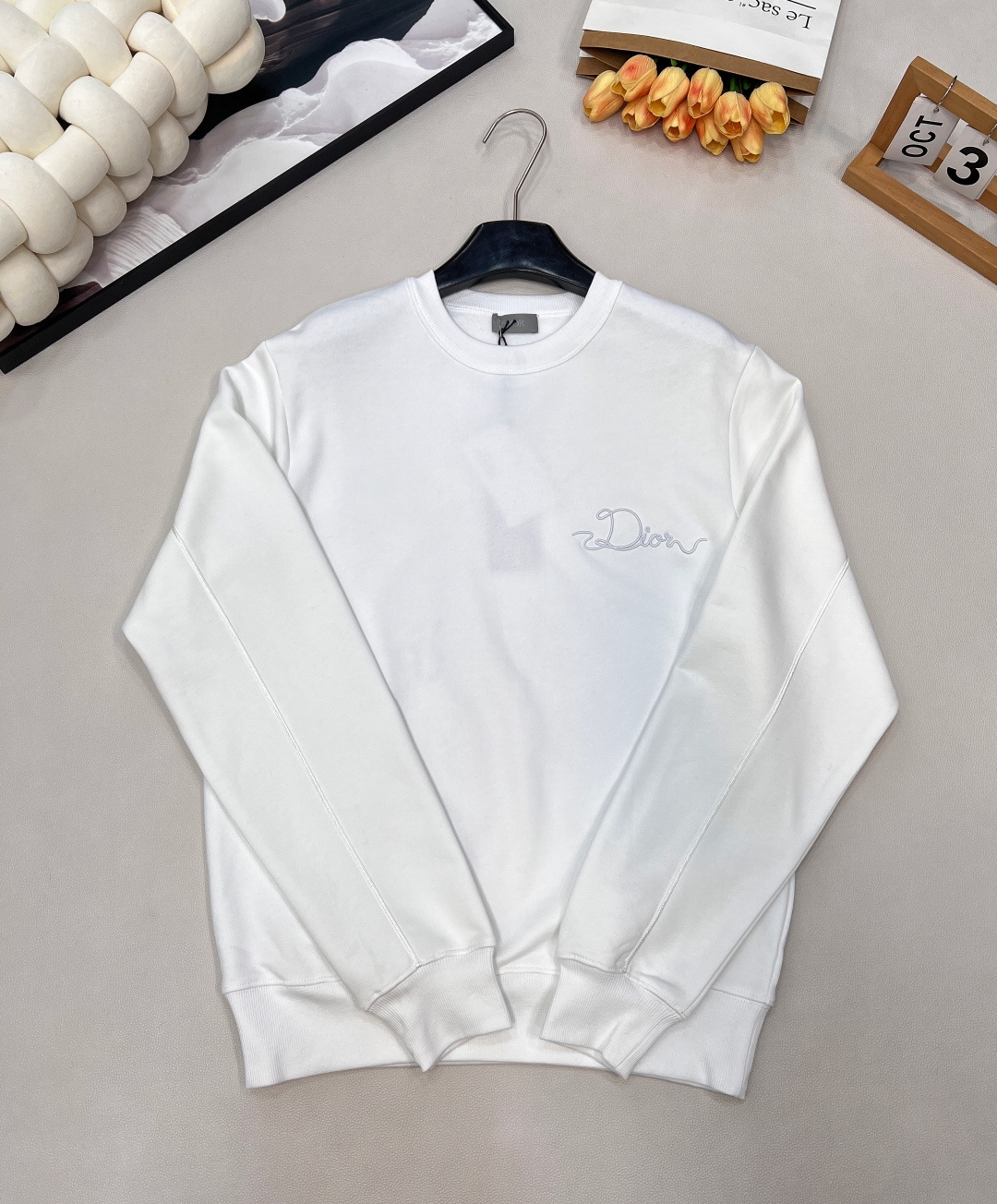 NO:590606,DIOR's new woven satin badge round neck sweatshirt, original 13, purchase; cotton pile terry fabric, ribbon letter embroidery, fabric using 26-count double-yarn terry fabric with base yarn, weight 380g/㎡; matched with 21-count 2x2 rib, composed of 95 cotton and 5 spandex; weight 380g/㎡. The 26-count double yarn is used as the surface yarn, and the yarn is thinner, ensuring the delicate and smooth appearance of the fabric and good color fastness; while the 10-count bottom yarn is used as the terry yarn, the yarn is thicker, and loose loops are formed during weaving. After unified raising or brushing treatment in the later stage, they are formed on the inside of the fabric. A layer of rich, dense and soft fluff. The high weight gives the sweatshirt a heavy drape and crisp texture, making it less prone to wrinkles and stronger styling capabilities. The pure cotton material ensures excellent breathability, moisture absorption and skin-friendly feel, and the final white color appears pure and rich in texture. Ribbon letter embroidery process, the ribbon itself has a silky luster and smooth touch, which is in sharp and high-end contrast with the matte plush feel of the sweater's suede surface. The embroidery decoration in the form of a ribbon is fixed on the fabric through special processing. The texture brought by this process is usually different from the woven texture and slight luster of the main knitted fabric. It forms an exquisite and accessible visual and tactile focus on the matte dark gray base, which enhances the craftsmanship design and uniqueness of the item. Loose round neck pullover sweatshirt with a webbing-covered back collar that is not easily deformed. The warm wrapping feel of the heavy fleece fabric, the stable closing of the strong elastic ribs and the logo embellishment create a lazy yet exquisite wearing experience. Its casual silhouette and white setting can easily create the popular relaxed look. Same style for men and women! Complete three standards, big shipments, size xssml code, dior, hoodie, sweatshirts, alexander wang19860909DIOR新款织缎徽章圆领卫衣,原13,购买；棉质起绒毛圈面料 、缎带字母刺绣、面料采用26支双纱支底纱的毛圈绒面料,克重380g/㎡；搭配采用21支 2x2 罗纹,成分為95棉与5氨纶；克重380g/㎡. 26支双纱作为表面纱线,纱线更细,确保了面料外观的细腻平整与良好的色牢度；而10支底纱作为毛圈纱,纱线更粗,在织造时形成松散的线圈,经后期统一的起绒或刷绒处理后,在面料内侧形成一层丰厚、浓密且柔软的绒毛.的高克重赋予了卫衣重磅的垂坠感和挺括的骨感,使其不易褶皱,造型能力更强.纯棉的材质保证了极佳的透气性、吸湿性和亲肤感,最终的白色呈现纯净且富有质感. 缎带字母刺绣工艺,缎带本身具有丝质的光泽与顺滑触感,与卫衣起绒面的哑光毛绒感形成鲜明而高级的对比.缎带形式的刺绣装饰,通过工艺特殊处理,使织带固定在面料上.这种工艺带来的质感通常是不同于主体针织面料的梭织质感与轻微光泽,在哑光的深灰色底上形成一个精致而触手可及的视觉与触觉焦点,提升了单品的工艺设计和独特性. 宽松圆领套头卫衣,后领人织带包领不易变形.重磅起绒面料的温暖包裹感、强弹性罗纹的稳固收口以及标志点缀,打造出一种慵懒而不失精致的穿着体验.其休闲廓形与白色设定,能轻松营造出当下流行的松弛感造型.男女同款！三标齐全,大货出 尺码xssml 编码,,dior,hoodie,sweatshirts,alexander wang,Women's clothing
