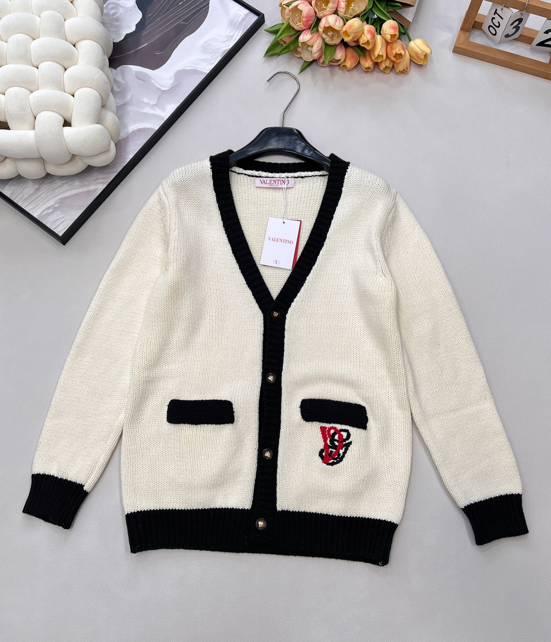 NO:652903,Valentino's new contrasting color V-neck knitted cardigan, the Italian elegance formula of white and black. When the milky white knitted material collides with the sharp black edges, Valentino weaves Italian elegance into daily life - the line of the V-neck is like a neat pen, tracing the slenderness of the neck; the black edge stitching and pocket trimming are the delicacy that cannot be hidden in minimalism.  The red and black 'V' logo on the pocket is the brand's recognition engraved in the stitching; the gold buckle closes lightly, and even the details are wrapped in low-key nobility. The wool knitted material is as soft as a cloud, and it feels uniquely gentle in autumn and winter when it touches the skin. The loose silhouette wraps up the looseness, but the ribs on the cuffs and hem contain the lazy border.  It is a 'universal outfit' that can be worn in all seasons. The suspenders inside give it a relaxed feel for afternoon tea. A stacked shirt brings sophistication to commuting. Even with jeans, it can be worn casually to create a haute couture atmosphere. From the stitching of the Italian workshop to the C position of the daily wardrobe, this cardigan welds the 'noble and unobtrusive' into autumn and winter outfits. It has three standards and is shipped in bulk. Size sml code, valentino, shirts, alexander wang19860909Valentino新款撞色V领针织开衫,白与黑的意式优雅公式 当奶白针织撞上利落黑边,Valentino把意式优雅织进了日常——V领的线条像一支利落的笔,描出脖颈的纤细；黑边锁边、口袋镶边,是极简里藏不住的精致. 口袋枚红黑交织的「V」标,是品牌刻在针脚里的辨识度；金扣轻合,连细节都裹着低调的贵气.羊毛针织料软得像云,贴肤时是秋冬独有的温柔,宽松廓形裹住松弛感,却又在袖口、下摆的罗纹里收住了慵懒的边界. 它是能穿四季的「万能搭子」内搭吊带是下午茶的松弛感,叠件衬衫就是通勤的精致,哪怕配条牛仔,也能把随性穿出高定氛围. 从意大利工坊的针脚到日常的衣橱C位,这件开衫把「贵气不张扬」焊在了秋冬穿搭里,三标齐全,大货出 尺码sml 编码,,valentino,shirts,alexander wang,Women's clothing