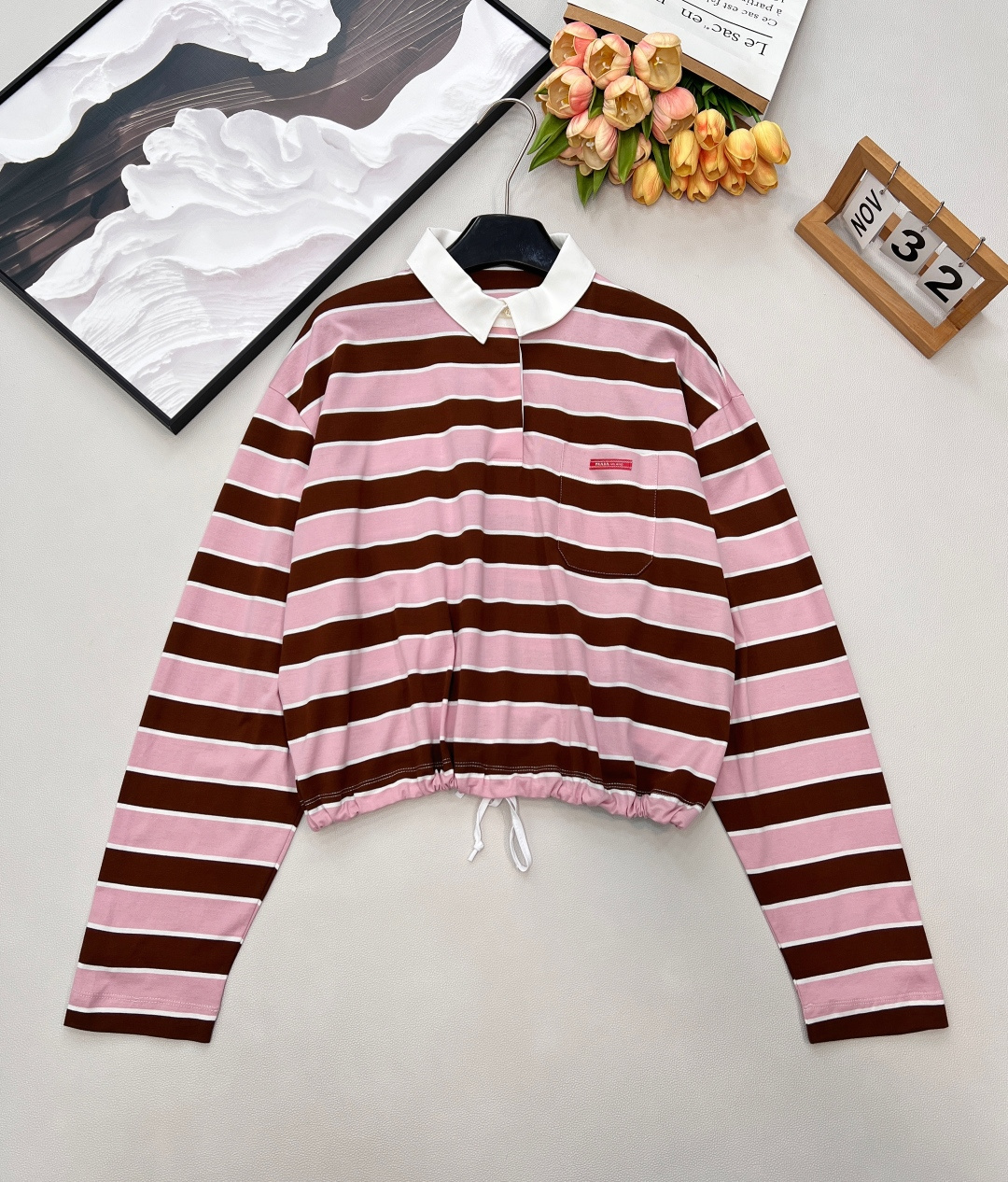 NO:716180,Prada26Ss early spring new retro striped POLO collar long-sleeved T-shirt丨exclusively developed by yb!  High quality production!  The iconic contrasting stripes have a relaxed retro feel, and the soft pink tones are intertwined with the mellow brown tones, weakening the toughness of the stripes and adding a gentle spring atmosphere. The classic POLO collar is paired with a slightly loose dropped shoulder cut, taking into account both casualness and exquisite details;  The drawstring design on the hem can be freely adjusted to create a lazy pleated or neat short style, suitable for layering or wearing alone. Selected breathable cotton fabrics, drape smoothly, can be easily controlled during daily commuting and weekend outings, complete with three standards, large quantities  Size sml code, prada, tees, t-shirt,19860909Prada26Ss早春新款复古条纹POLO领长袖T恤丨独家yb开发！高版出品！标志性的撞色条纹自带松弛复古感,柔和的粉调与醇厚的棕调交织,弱化了条纹的硬朗感,更添春日温柔氛围.经典POLO领搭配微宽松落肩剪裁,兼顾休闲随性与精致细节；下摆抽绳设计可自由调节松紧,打造慵懒堆褶或利落短款两种造型,适配叠穿或单穿需求.精选透气棉感面料,垂坠顺滑,日常通勤、周末出街皆可轻松驾驭,三标齐全,大货出 尺码sml 编码,,prada,tees，t-shirt,,Women's clothing