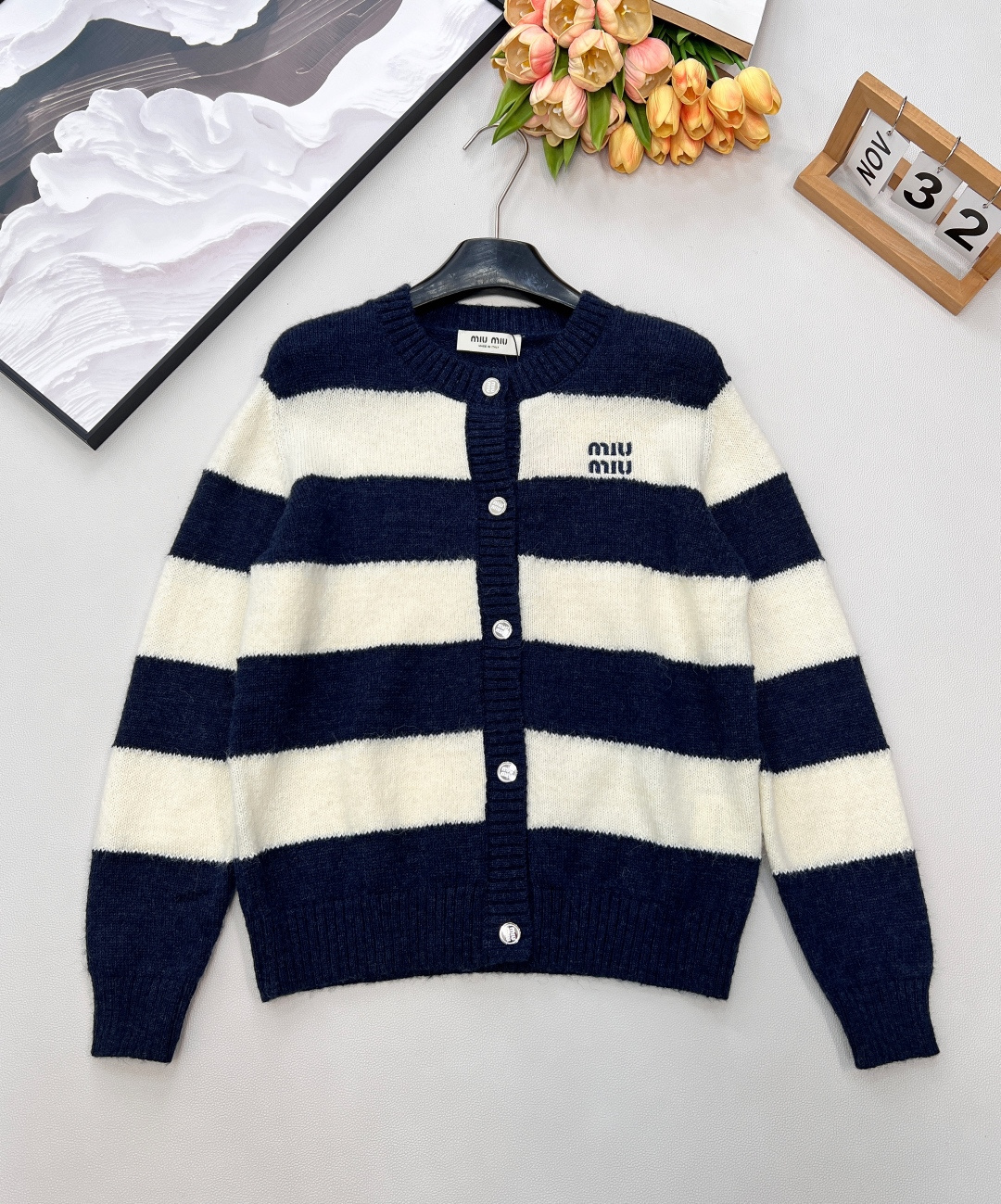 NO:734933,Miu Miu 26 new early spring knitted cardigan, made of soft and skin-friendly wool blend fabric, is not tied at all when worn close to the body, and gently wraps every inch of the skin in spring. Classic wide stripes with contrasting color splicing, evenly proportioned, visually slimming in a second, hiding the flesh and making it more neat. The iconic 'miu' letter embroidery on the left chest is exquisite and self-recognizable, and it is matched with metal buttons with full luster, showing a light and luxurious style in every detail.  The versatile version of round neck + long sleeves is gentle when worn alone or eye-catching when layered. Whether worn with jeans for a relaxed feel or with a skirt for a college style, you can easily create a fashionable atmosphere. Complete with three standards and two colors. Size sml code M,,miumiu,skirts,jeans,19860909Miu Miu 26早春新款针织开衫,软糯亲肤的羊毛混纺面料,贴身穿完全不扎,温柔包裹住春日的每一寸肌肤. 经典宽条纹撞色拼接,比例均匀恰到好处,视觉上一秒显瘦,藏住肉肉的同时更显利落感. 左胸标志性“miu”字母刺绣,精致细腻自带辨识度,搭配光泽感满分的金属纽扣,细节处尽显轻奢格调. 圆领+长袖的百搭版型,单穿温柔、叠穿点睛,无论是配牛仔裤打造松弛感,还是搭半裙走学院风,都能轻松拿捏时髦氛围.三标齐全,两色出 尺码sml 编码M,,miumiu,skirts,jeans,,Women's clothing