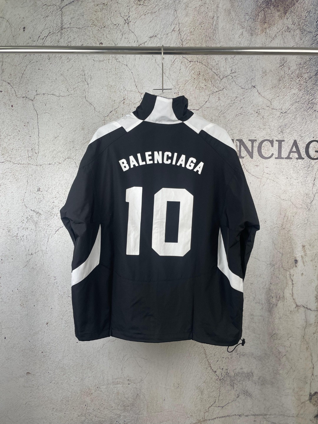 💰175 【原版】款号：AB035
【上新】Balenciaga丨 巴黎世家 23SS 联名足球背后字母印花冲锋衣立领外套

引入足球元素 黑白配色字母印花设计 宽松版型 双向拉链闭合 前胸sponsor刺绣徽章 后背压印徽标及球队号码 动感活力的一款冲锋衣

os宽松版型 双层用料 整件用布5米 成本极高 由47块裁片组成  出品极慢 绝对重工 整件车缝止口需要车的很均匀平整否则就拼不起来成品，特别是不规则的拐弯处还得左右对称裁片，如果线路没控制好很容易出现裁片长短 还有前幅印花位需左右平齐对称 左袖口带有新款定制足球刺绣徽章

颜色：黑
Size：S M L XL 现货秒发 详细尺码可查图9
